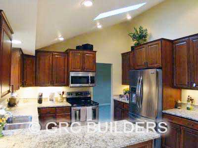 Kitchen featuring skylights, recessed lights, stainless steel appliances and dark cabinetry.
